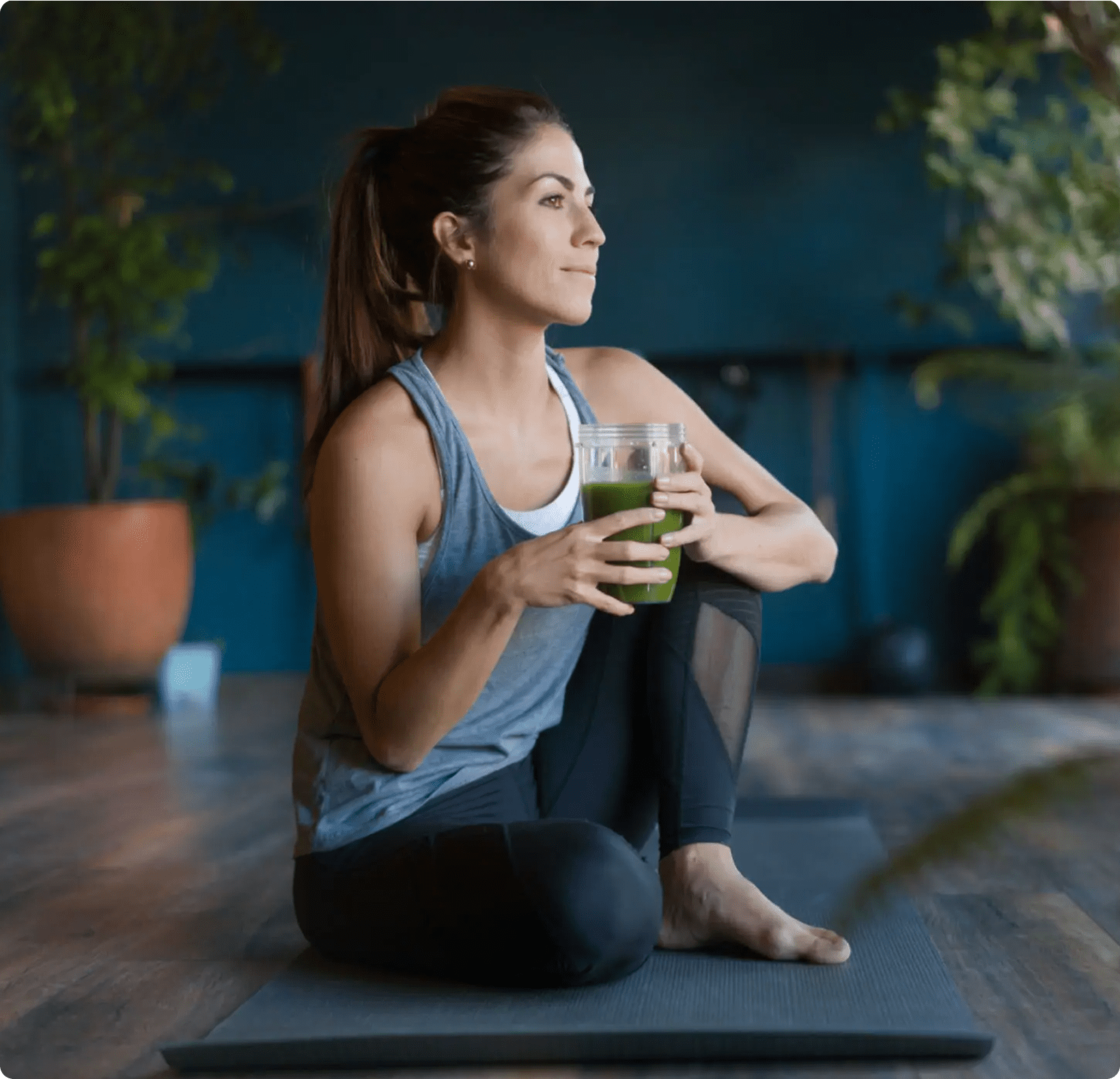 Woman on yoga mat holding green smoothie