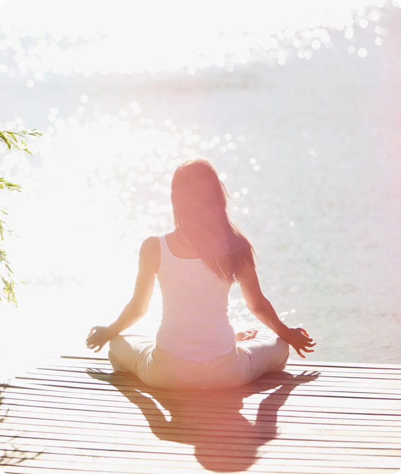 Person meditating on dock by sparkling water