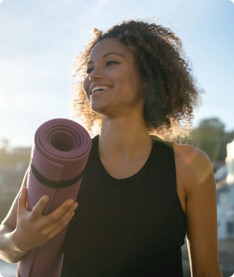 Smiling woman holding purple yoga mat outdoors